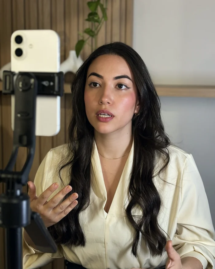 Mulher sentada num café, gesticulando enquanto fala para o celular no tripé