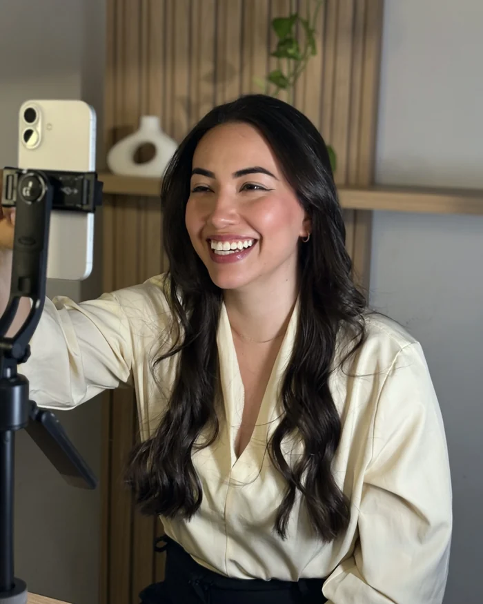 Mulher sorrindo e ajustando o celular no tripé antes de gravar