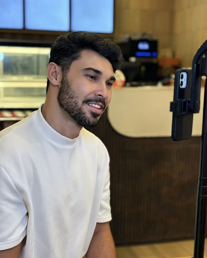 Homem sentado num café, falando de perto para o celular no tripé